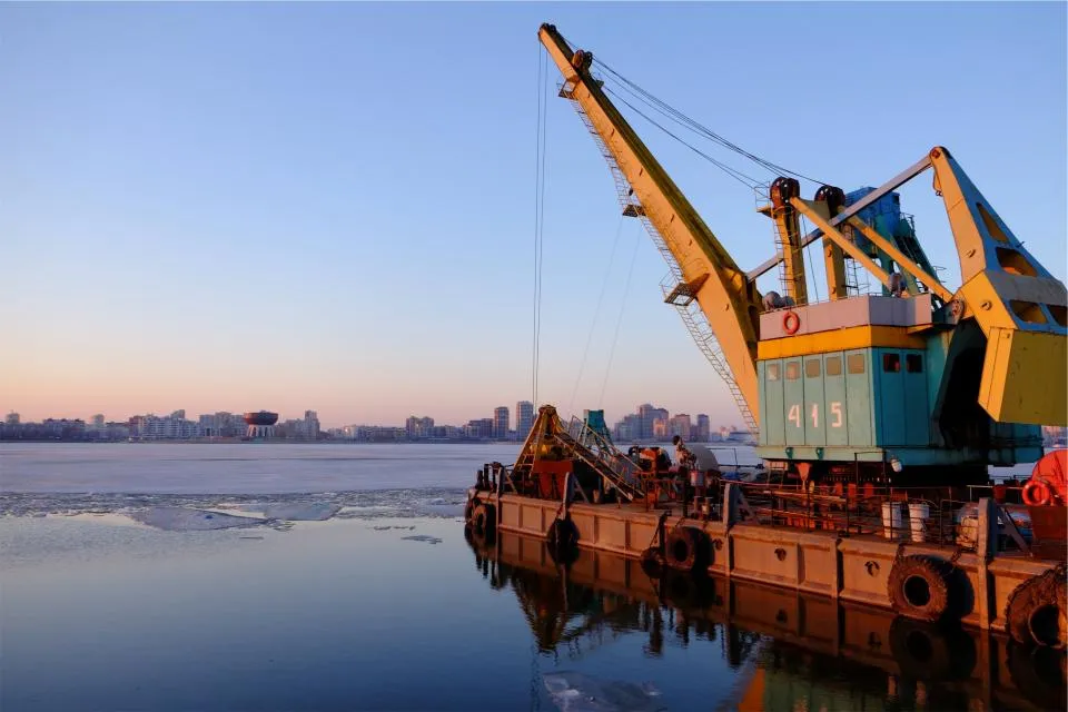 A harbour crane on a barge beside sea ice in a cold northern port at dusk